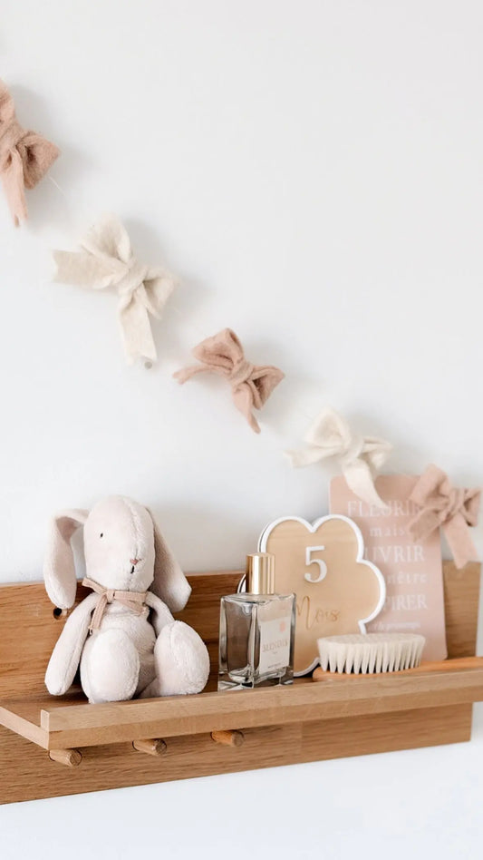 Guirlande de nœuds écru et rose poudré en laine feutrée, décoration artisanale pour chambre de bébé.